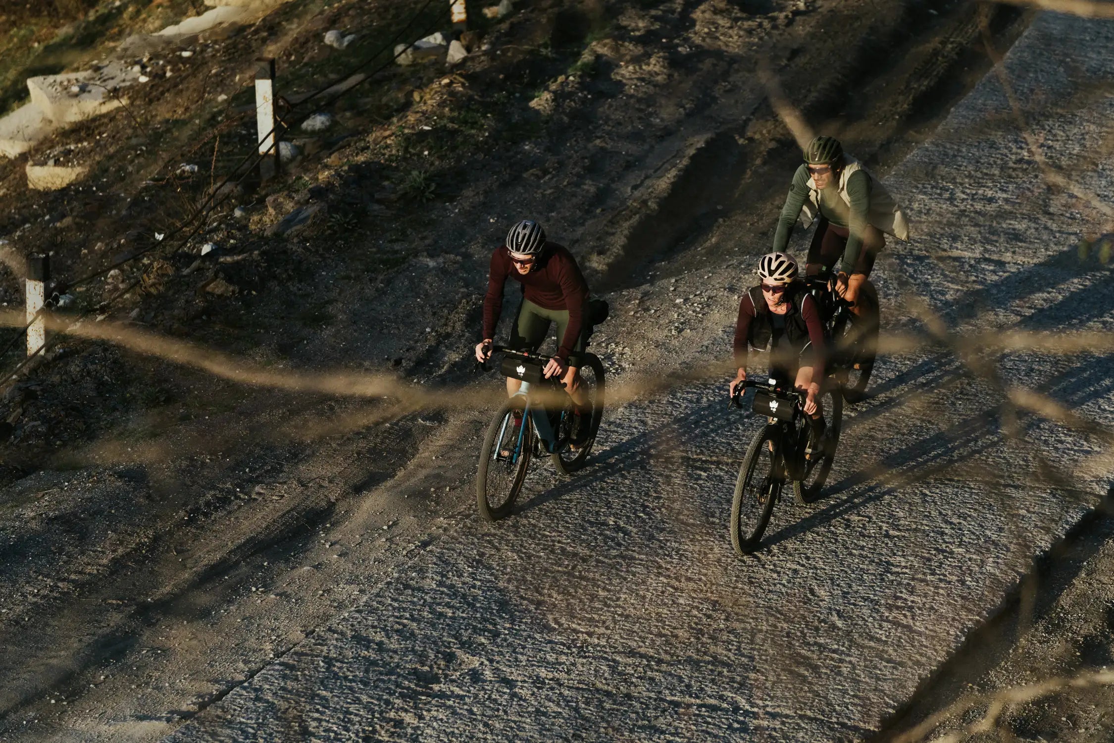 Three cyclists riding a gravel road at sunset